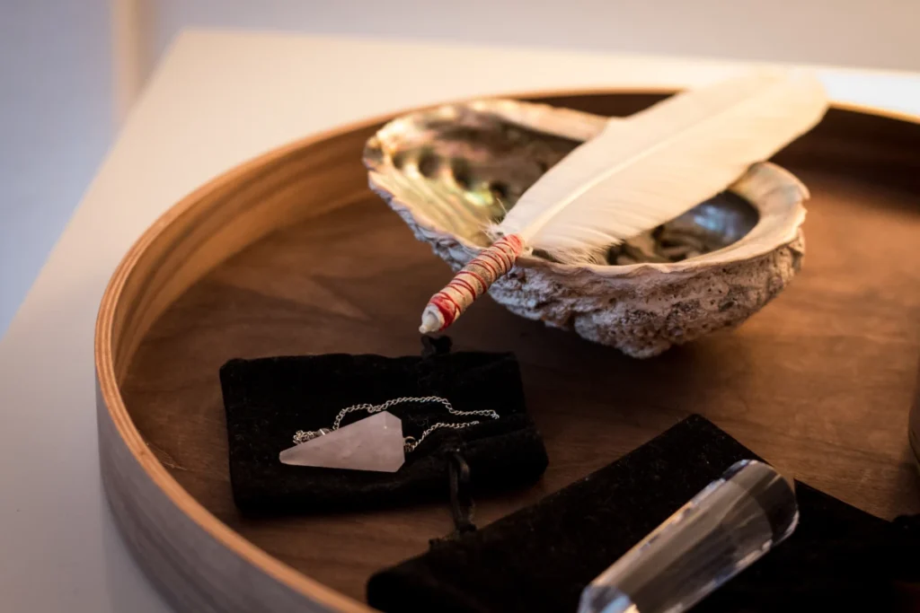 Weiße Feder, Muschel und Kristall auf einem Holztablett