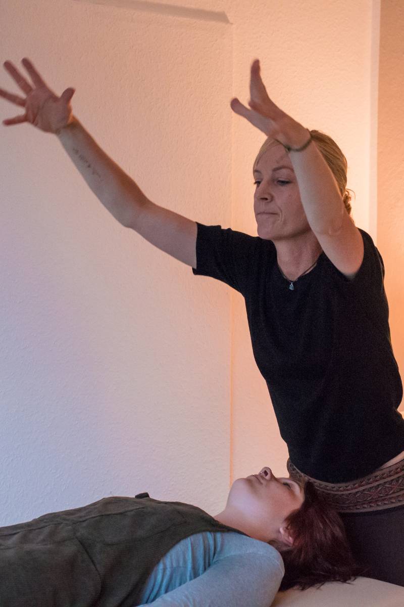 Miriam mit ausgestreckten Armen über Klientin auf der Liege gebeugt