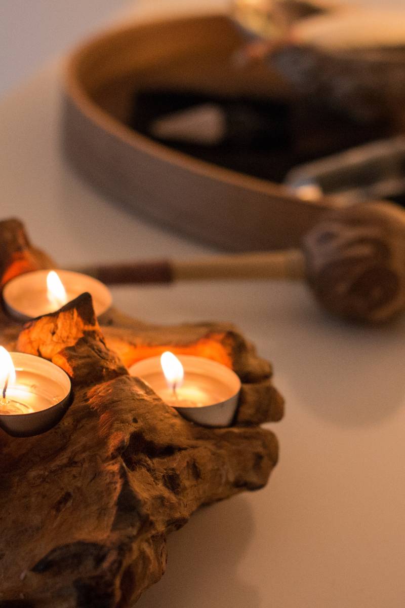 Teelichter auf einer Wurzel, dahinter unscharf eine Rassel und ein Tablett